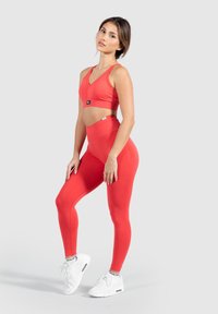 Roter Sport-BH und hochtaillierte Leggings aus dehnbarem Material. Der BH hat ein V-Ausschnitt-Design, und beide Teile besitzen eine glatte Textur.