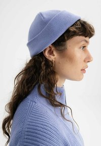 Lichtblauwe gebreide beanie met een opgerolde zoom, gedragen door een persoon met golvend bruin haar. De stof heeft een geribbelde textuur voor isolatie.