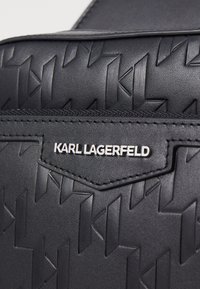 Black textured handbag featuring a raised geometric pattern, a silver logo tag, and a smooth accent at the top.