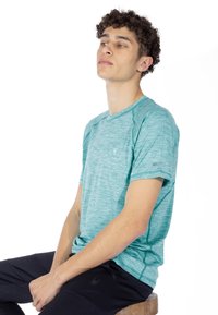 Turkos tränings t-shirt med en texturerad design, korta ärmar, platta sömmar och en liten logotyp på bröstet; matchas med mörka byxor.