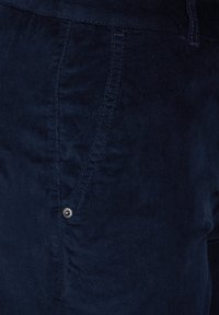 Mörkblå kordflossabomull med en subtil lyster, med synliga sömmar och en metalldetalj med knapp vid sömmen.