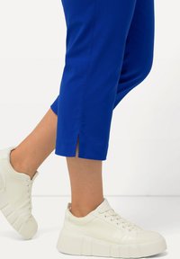 Pantaloni cropped blu con aperture laterali all'orlo, abbinati a sneakers bianche chunky con una tomaia texture e una suola spessa.