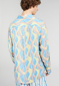 Camicia a maniche lunghe colorata con un motivo ondulato in blu, rosa e giallo su uno sfondo chiaro. Tessuto morbido e liscio con colletto.