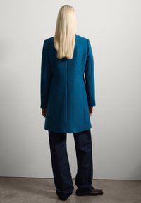 Teal wollen jas met lange mouwen, op maat gemaakt silhouet en een rechte snit, gecombineerd met donkere denim broeken en bruine schoenen.