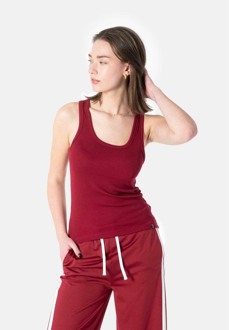 Rød ribbet tanktopp med scoop-hals, tettsittende design og brede stropper, kombinert med matchende røde vide bukser med hvite snor.