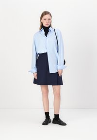 Vaaleansininen nappipaita, musta poolopaita, tummansininen hame, mustat loafer-kengät, kerrokselliset sukat. Minimalistinen muotoilu yhtenäisellä taustalla.
