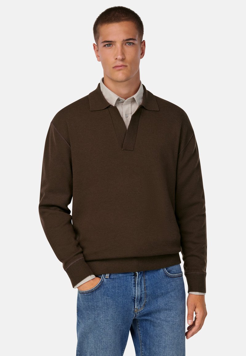 Pruun pullover-sviiter, millel on krae ja ribidega mansetid ning äär. Kandes heledat halli kraega särki, koos siniste teksadega.