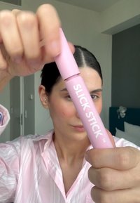 Slick Stick-produkt i rosa förpackning, cylindrisk form, med fet vit text; hålls i handen för att visa design och användbarhet.