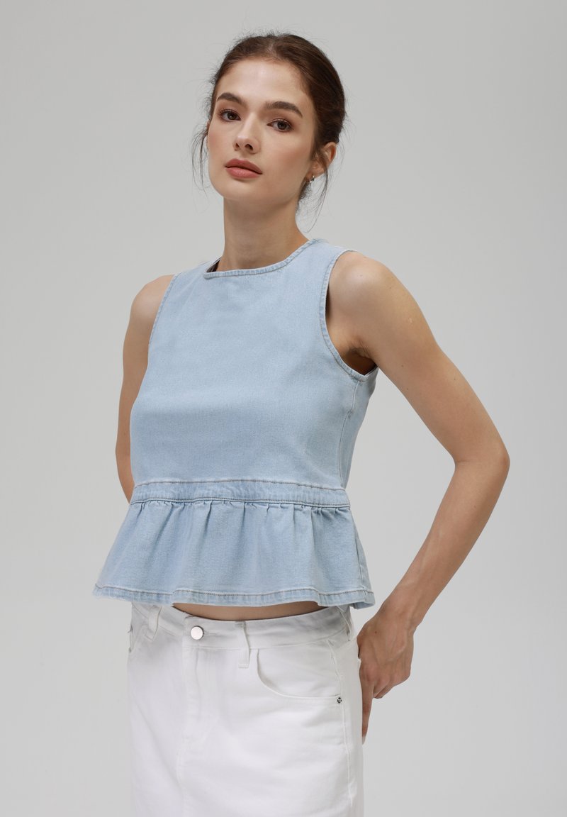Lyseblå denim uten ermer med peplumdesign og sydd detaljer, kombinert med hvite bukser. Glatt tekstur, uformell passform.