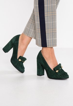 Groene suède pumps met een ronde neus, voorzien van een decoratieve franjerand en gouden accenten, gecombineerd met een stevige hak.