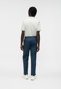 Ανοιχτό γκρι πόλο μπλουζάκι με κοντά μανίκια, σε συνδυασμό με σκούρο μπλε παντελόνι. Το μοντέλο στέκεται με την πλάτη στραμμένη, αναδεικνύοντας τη φόρμα και το χρώμα του ρούχου.