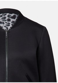 Schwarze Zip-Jacke mit rundem Kragen und Leopardenmuster-Futter, das am Hals sichtbar ist.