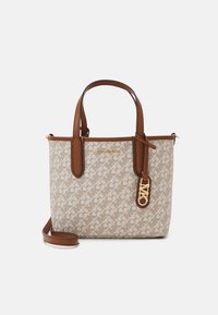 Michael Kors beige olkanen laukku, jossa on logoprintti ympäriinsä, ruskeat nahkahihnat ja irrotettava olkahihna valkoista taustaa vasten.