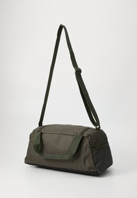 Grønn duffelbag laget av slitesterkt stoff, med to håndtak, justerbar skulderrem og en strukturert meshpanel på den ene siden.