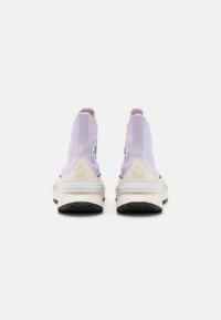 Sneaker alte in tessuto lavanda chiaro con dettagli bianchi, dotate di un logo circolare e di una suola in gomma nera texture.