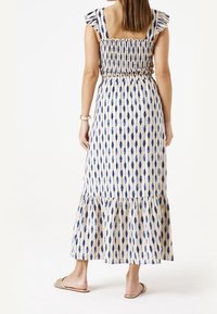 Maxi sukienka z marszczonym gorsetem, falbaniastymi ramiączkami i rozkloszowaną spódnicą z niebiesko-beżowym wzorem wydłużonych kształtów.