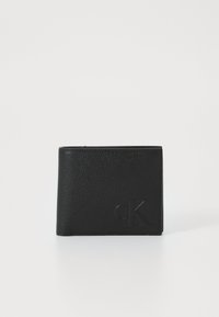 Portafoglio in pelle nera con superficie texture, design pieghevole a due scomparti e logo "cK" in rilievo sulla parte anteriore. Forma compatta e minimalista.