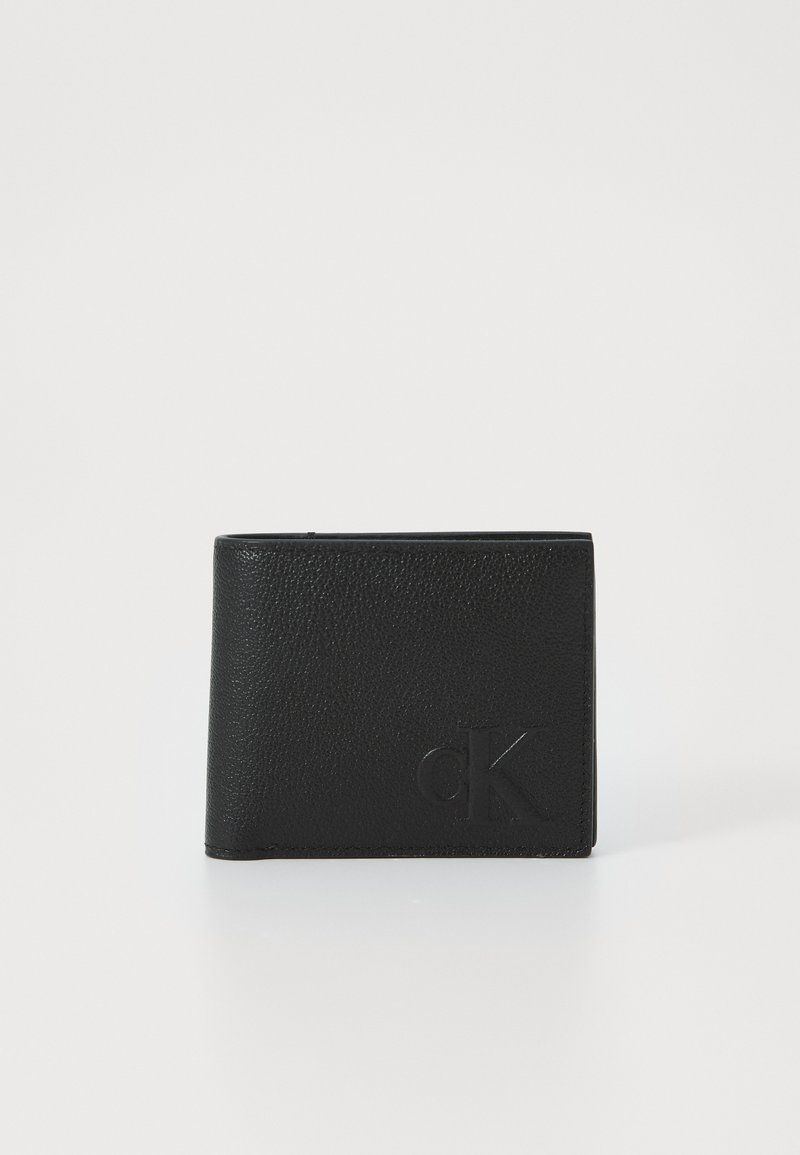 Portafoglio in pelle nera con superficie texture, design pieghevole a due scomparti e logo "cK" in rilievo sulla parte anteriore. Forma compatta e minimalista.