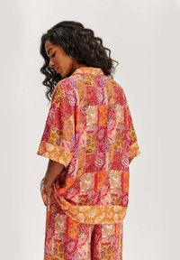 Pestrá patchwork košeľa s paisley a kvetinovými vzormi, krátkymi rukávmi a jasne oranžovým golierom a lemami. Ľahká látka.