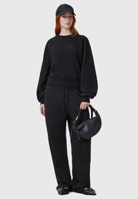 Conjunto de sudadera y pantalones negros, con un corte relajado, escote redondo y acabado texturizado. Combinado con una gorra negra y un bolso pequeño.