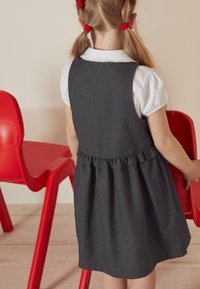 Gray dress with a ruffled hem and a white collared shirt underneath. Child holding a red plastic chair in background.