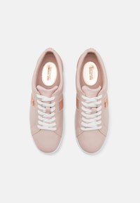 Jasnoróżowe trampki z białymi sznurowadłami, gładką skórą i siateczkowymi akcentami, z metalicznym logo i płaską białą podeszwą.