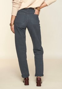 Pantalones grises de pierna recta con puños enrollados, dos bolsillos traseros y una textura suave, combinados con zapatos de tacón marrón oscuro.