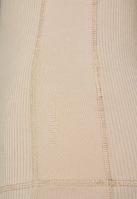 Tessuto beige di Calvin Klein con una texture rigata, una cucitura liscia e un logo in rilievo, che mette in evidenza il suo design minimalista.