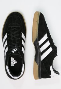 Black suede athletic shoes with white three-stripe design, black laces, and a gum rubber sole. Features a padded collar and logo on the tongue.