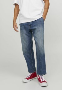 Vaqueros de mezclilla azul de pierna recta con un acabado desvanecido, combinados con una camiseta blanca holgada y zapatillas rojas de caña alta.