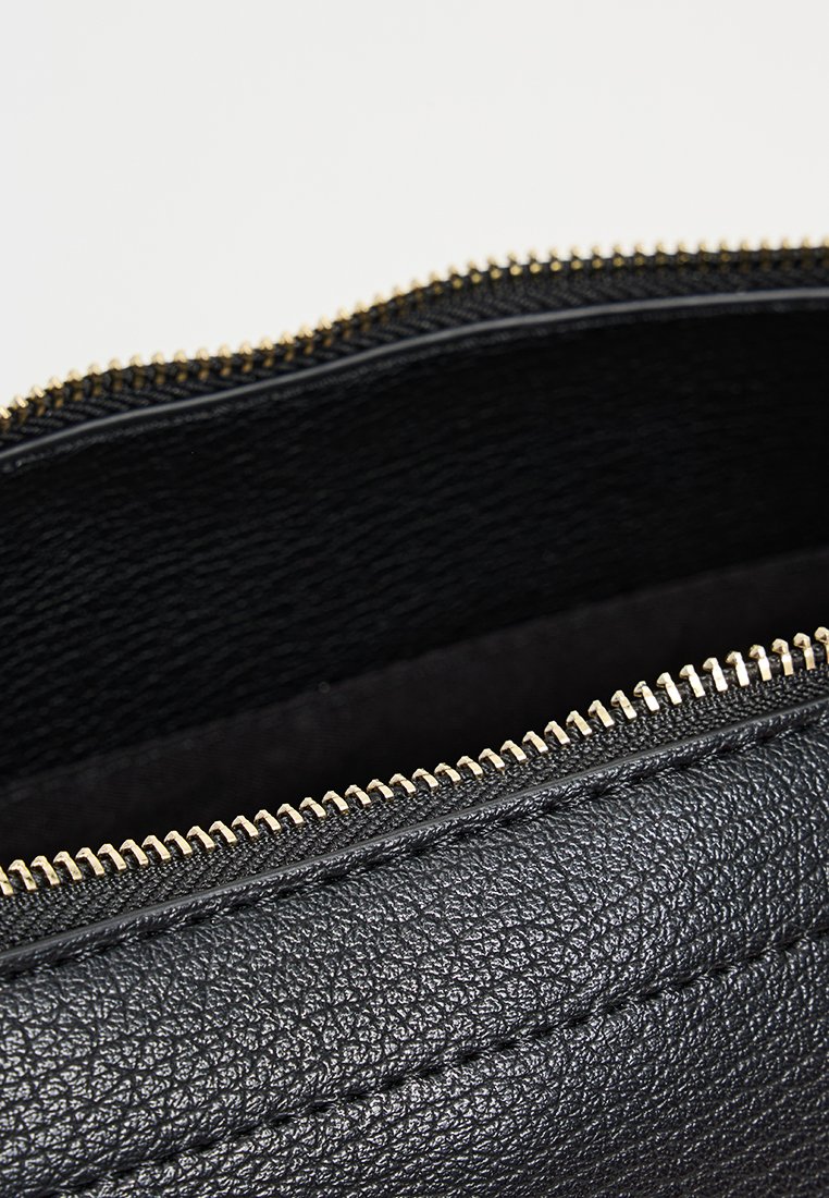 Sac en cuir noir avec une surface texturée, doté d'une fermeture éclair dorée et de coutures. L'intérieur est doublé de tissu noir.