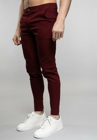 Pantalons ajustés bordeaux avec deux poches avant et une fermeture à bouton. Portés avec des baskets blanches dotées d'une semelle texturée et d'un design à lacets.