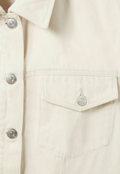 Camisa de mezclilla en beige claro con botones plateados, bolsillo en el pecho con solapa y acabado texturizado en la tela.