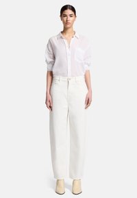 Biała koszula z guzikami, z kieszonką z przodu i podwiniętymi rękawami, połączona z białymi spodniami o wysokim stanie i szerokimi nogawkami oraz kremowymi botkami do kostek.