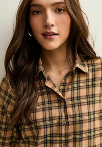 Bruin geruit flanellen overhemd met zwarte en gele lijnen, knopen aan de voorkant en een klassieke kraag. Zachte textuur, casual ontwerp.