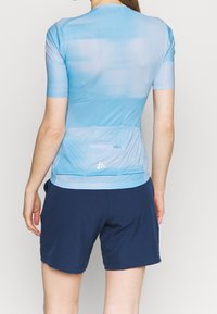 Ljusblå träningsskjorta med kort ärm, gradientdesign, rundad halsringning och detalj med bakficka, i kombination med marinblå shorts.