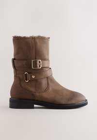 Bottine en cuir marron avec boucle latérale et détail de sangle. Présente une finition texturée, un bout arrondi et un petit talon noir.