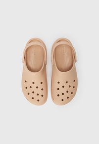 Peach-colored Crocs clogs with ventilation holes, soft textured material, back strap, and a contoured footbed for comfort.