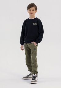 Zwarte sweatshirt met witte ronde hals, groene sweatpants en hoogtop sneakers in grijs en zwart; heeft logo-accenten op de sweatshirt en broek.