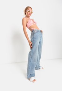 Svetlo modri široki jeans, v kombinaciji z roza vzorčasto topom z obročem in belimi sandali s peto. Dodatki vključujejo velike sončne očala v rumenih tonih.