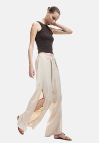 Top nero senza maniche abbinato a pantaloni larghi color crema con fessure laterali e vita annodata; modella che indossa sandali flats.