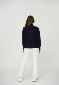 Maglione a collo alto navy con una texture a coste, abbinato a pantaloni bianchi a zampa d'elefante, caratterizzati da una vestibilità affusolata e spacchi all'orlo.