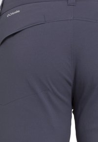 Närbild av mörkgrå Columbia-byxor som visar detaljer på bakfickan och midjebandet.