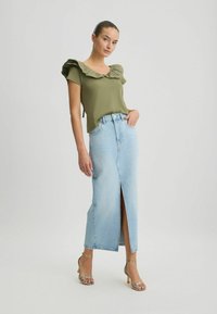 Oliven grøn top med rynket udskæring, parret med en lyseblå denim-maxinederdel med slids foran, suppleret af stropede hælsandaler.