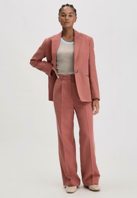 Roze fonkelende maatpak met een blazer met één knoop, brede broekspijpen en een lichtbeige top met een blauwe geribbelde kraag.