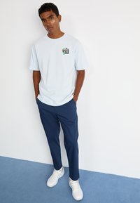 Lyseblå t-shirt med grafisk tryk foran, parret med marineblå bukser og hvide sneakers. Enkel design, løs pasform og glat stof.