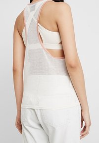 Vit meshlinne med ljusrosa detaljer. Har en avslappnad passform, öppen ryggdesign och synliga band undertill. Texturerad tyg.