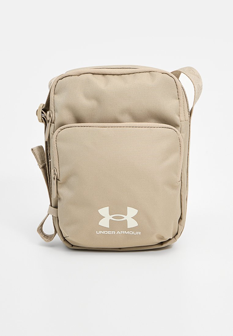 Sacoche crossbody beige Under Armour en tissu durable ; comporte une poche avant, une bandoulière réglable et un logo imprimé en blanc. Design compact.