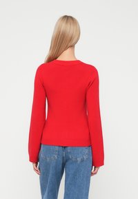 Red sweater with a round neck and long sleeves, textured knit material, ribbed hem, paired with light blue high-waisted jeans.