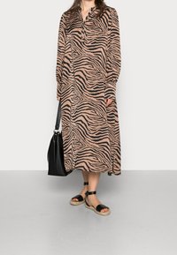 Lång, knappad klänning i zebramönster med nyanser av beige och svart. Matchas med svarta espadrillos och en svart axelväska.